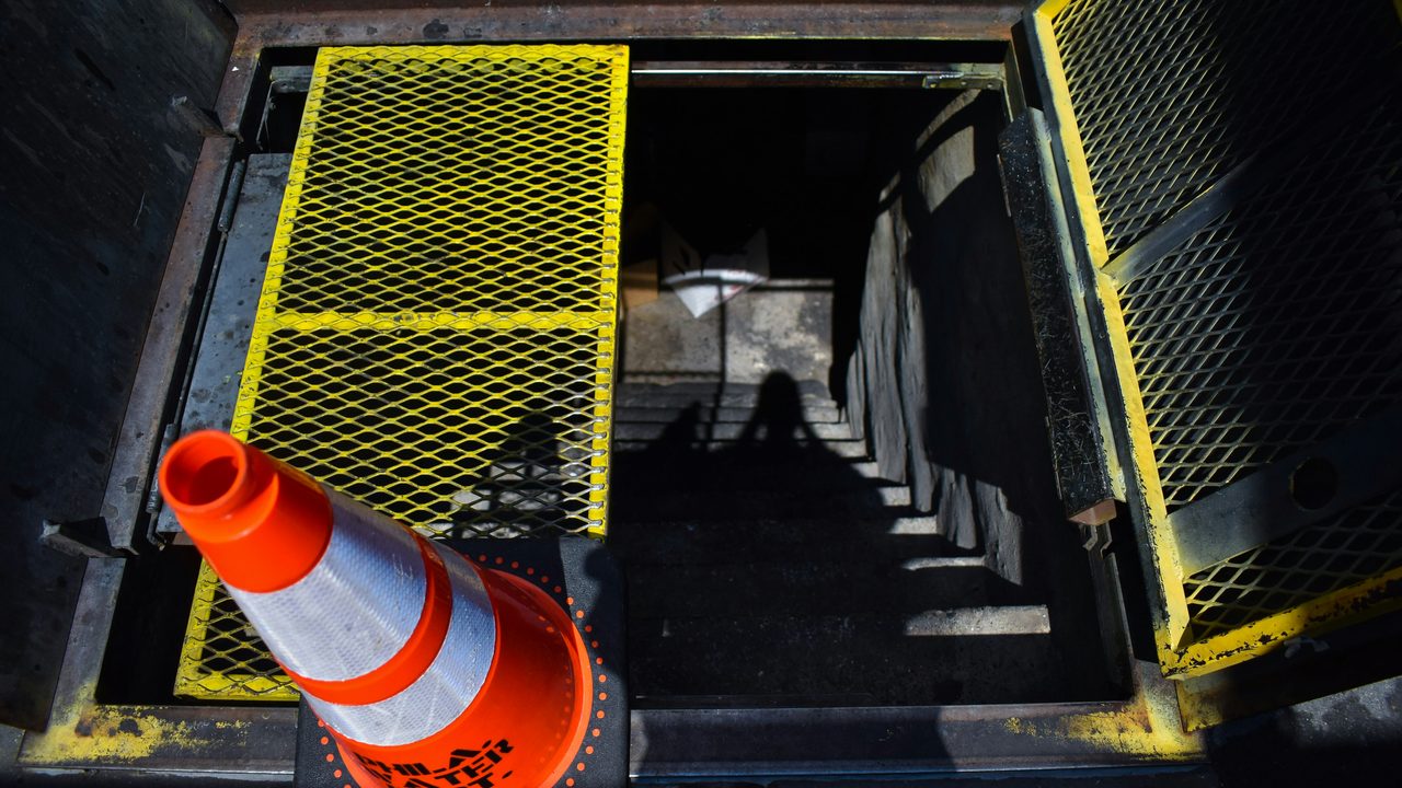Open access hatch into an underground vault, guarded with mesh panels and a traffic cone