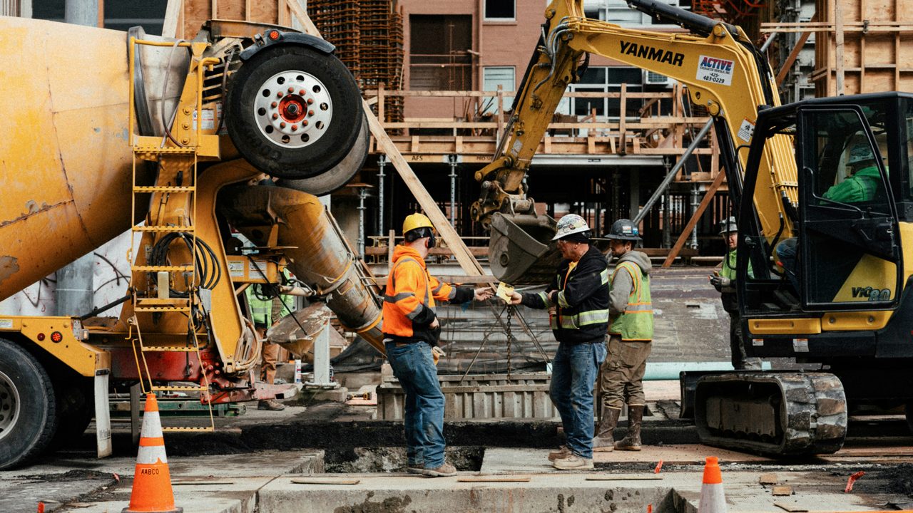 Site workers in hi-vis conferring beside a concrete truck and excavator